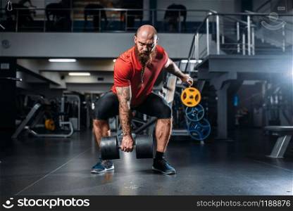 Athletic male lifter doing exercise with dumbbells in gym. Bearded sportsman in sport club, healthy lifestyle