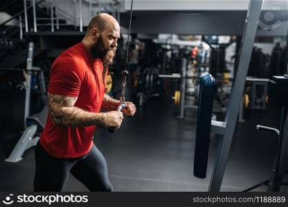Athletic male person in sportswear, training on exercise machine in gym. Bearded man on workout in sport club, healthy lifestyle. Athletic male person, training on exercise machine