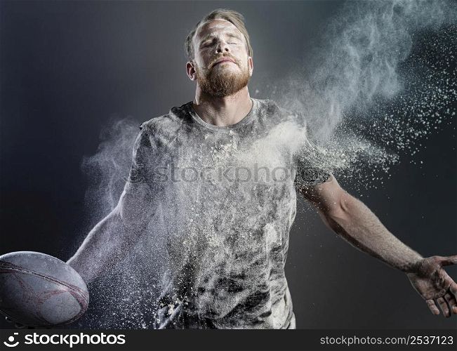 athletic male rugby player holding ball with powder