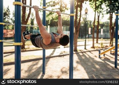 Athletic man doing exercise on press using horizontal bar, outdoor fitness workout. Strong sportsman on sport training in park