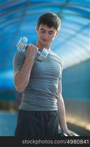 Athletic man doing exercises with dumbbells outdoors in city