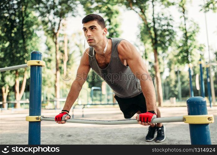 Athletic man doing push-up exercise using horizontal bar, outdoor fitness workout. Strong sportsman on sport training in park. Man doing push-up exercise using horizontal bar