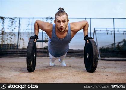 Athletic man doing push-up exercise with weights, street workout, crossfit. Fitness training on sports ground outdoor, male person pumps muscles, active urban lifestyle. Man doing push-up exercise, street workout