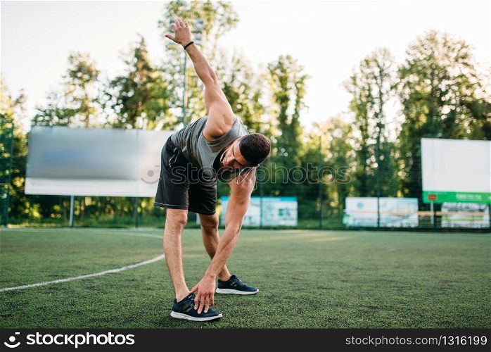 Athletic man doing stretching exercise, side view, outdoor fitness workout. Strong sportsman in park