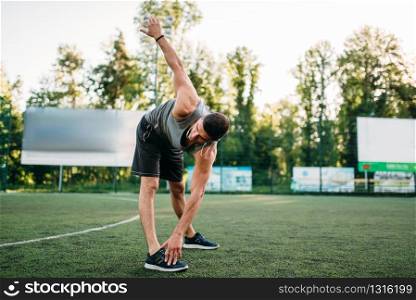 Athletic man doing stretching exercise, side view, outdoor fitness workout. Strong sportsman in park