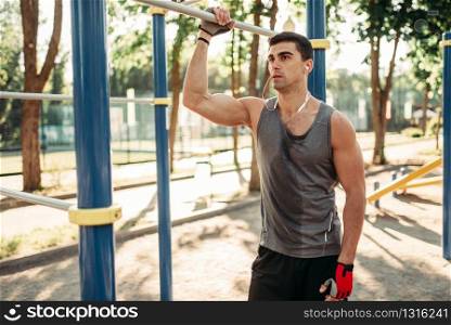 Athletic man pulled up on one hand, exercise on horizontal bar, outdoor fitness workout. Muscular sportsman on sport training in park. Athletic man pulled up on one hand outdoor