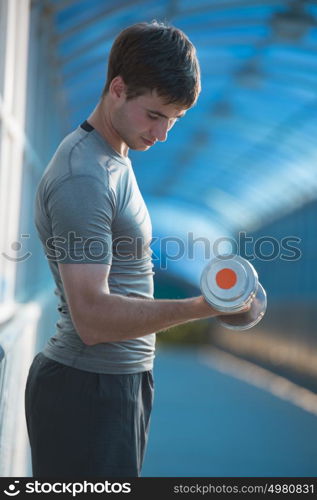 Athletic man pumping up muscles with dumbbells outdoors in city