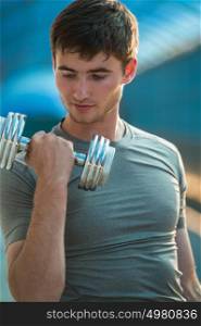 Athletic man pumping up muscles with dumbbells outdoors in city
