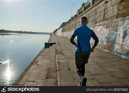 Athletic man running and doing functional workout outdoors. Sportive adult male in sportswear training in city on river bank. Back view. Athletic man running and doing functional workout outdoors