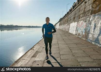 Athletic man running and doing functional workout outdoors. Sportive adult male in sportswear training in city on river bank. Athletic man running and doing functional workout outdoors