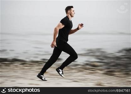 Athletic man running by the rocky seaside coast.. Athletic man running by the rocky seaside coast
