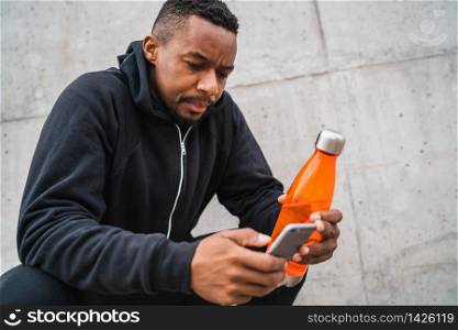 Athletic man using his mobile phone and holding a bottle of water after training against grey background. Sport and health lifestyle.