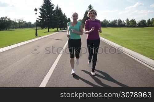 Athletic mature exhausted women in sportswear resting during jogging. Tired senior female joggers taking deep breath and resting while they stopped on park road. Sporty senior females resting with hands on knees. Slow motion. Stabilized shot.
