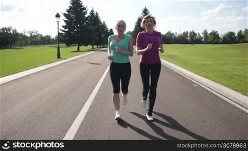 Athletic mature exhausted women in sportswear resting during jogging. Tired senior female joggers taking deep breath and resting while they stopped on park road. Sporty senior females resting with hands on knees. Slow motion. Stabilized shot.