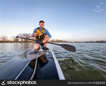 athletic senior man on a stand up paddleboard enjoying sunset lover a calm lake in Colorado, bow view