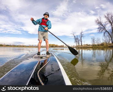 athletic senior man on a stand up paddleboard on a calm lake in Colorado, bow view