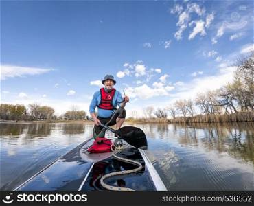 athletic senior man on a stand up paddleboard on a calm lake in Colorado, bow view