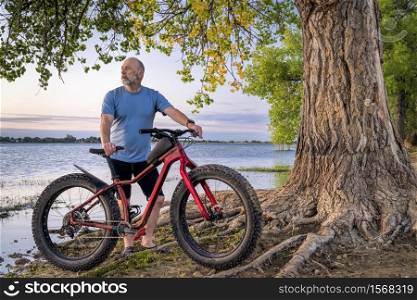 athletic senior man with a fat mountain bike on a lake shore enjoying sunrise - Boyd Lake State Park in northern Colorado