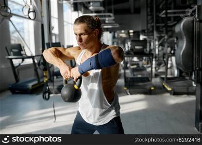 Athletic sportsman in sportswear doing squats with medicine balls at gym. Fitness training and healthy lifestyle concept. Handsome muscular man doing cross fit training with kettle bell lifting at gym
