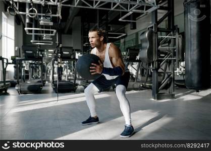 Athletic sportsman in sportswear doing squats with medicine balls at gym. Fitness training and healthy lifestyle concept. Athletic sportsman in sportswear doing squats with medicine balls at gym