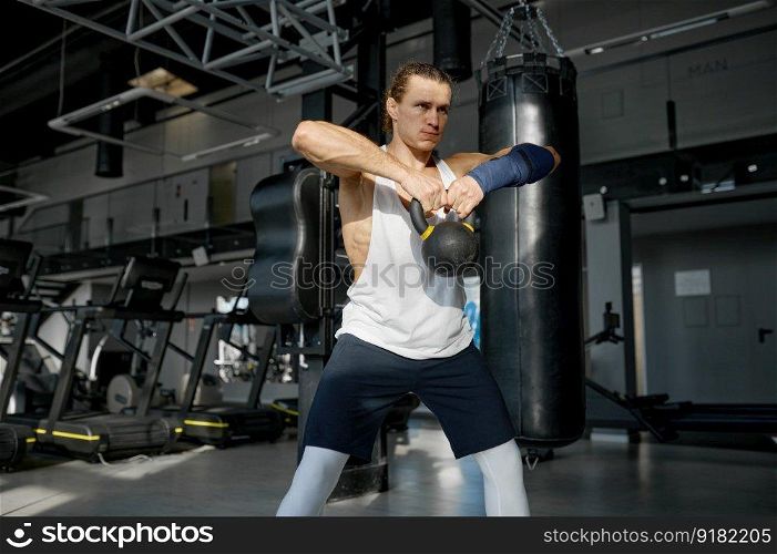Athletic sportsman in sportswear doing squats with medicine balls at gym. Fitness training and healthy lifestyle concept. Handsome muscular man doing cross fit training with kettle bell lifting at gym