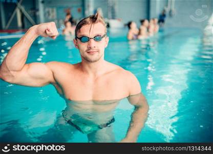 Athletic swimmer shows muscles, indoor swimming pool. Aqua sports exercise. Athletic swimmer shows muscles, aqua sports