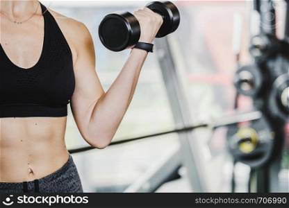 Athletic woman doing biceps muscle workout with dumbbell in close-up at the gym ( copy space).