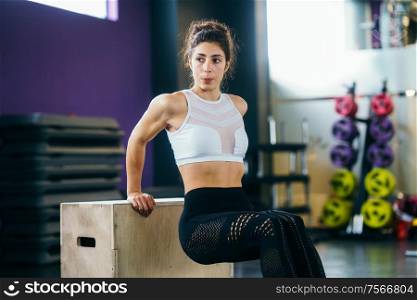 Athletic woman doing triceps push-ups with a wooden box at the gym.. Athletic woman doing triceps push-ups at the gym.