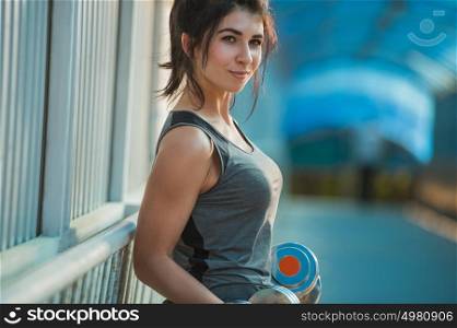 Athletic woman pumping up muscles with dumbbells outdoors in the city