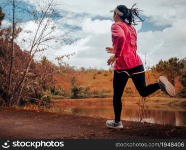 Athletic woman running on forest trail by the lake. Female runner running in nature in the morning. Workout Healthy lifestyle concept.