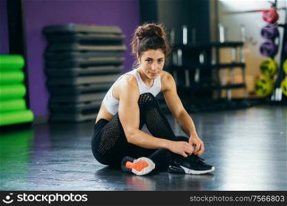 Athletic woman tying her sneakers sitting on the gym floor. Athletic woman tying her sneakers at the gym