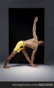 Athletic yoga doing stretching exercise in studio, grey background. Strong man practicing yogi , asana training, top concentration, healthy lifestyle. Athletic yoga doing stretching exercise in studio