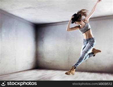 Athletic young dancer jumping on a concrete wall background