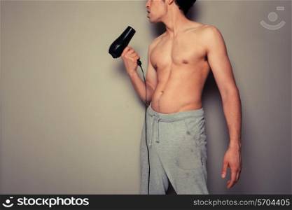 Athletic young man is holding a hair dryer and messing around with it