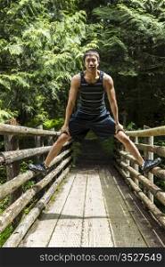 Athletic young man straddling walkway bridge into woods