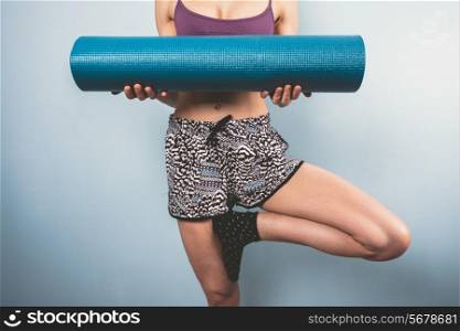 Athletic young woman in a tree pose is holding a yoga mat