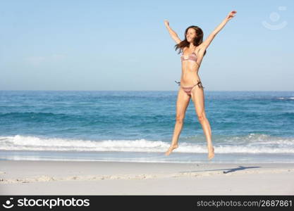 Athletic Young Woman Jumping On Sandy Beach On Holiday Wearing Bikini