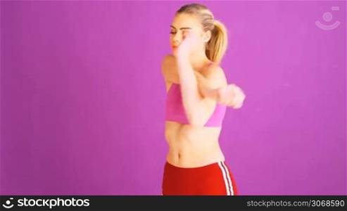 Athletic young woman stretching before exercising raising her arms behind her head in sportswear on a purple studio background with copyspace