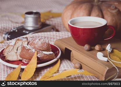 atmospheric autumn background cup of coffee, bun, pumpkin, apples, book, headphones, retro camera