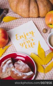 atmospheric autumn background pumpkin, apples, coffee, bun, autumn leaves with the inscription enjoy every day of your life