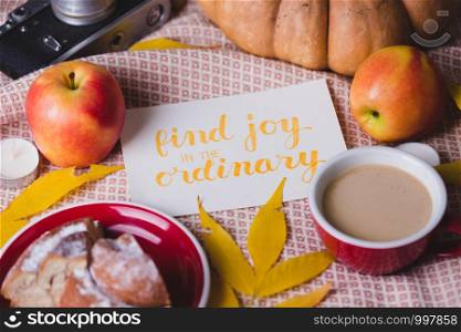atmospheric autumn background pumpkin, apples, coffee, bun, autumn leaves with the inscription find joy in the ordinary