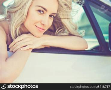 Atmospheric outdoors fashion portrait of beautiful blonde in car on the beach
