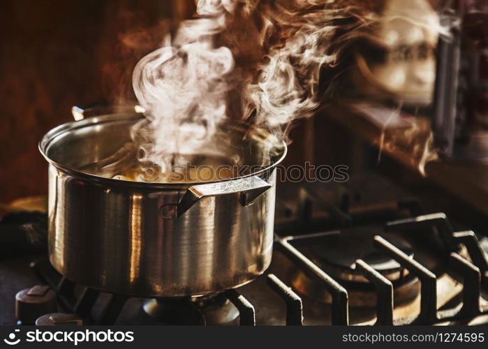 Atmospheric shot of beautiful clouds of steam rising from water boiling in a stainless steel cooker placed on a dusty cook-top