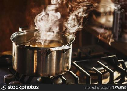 Atmospheric shot of beautiful clouds of steam rising from water boiling in a stainless steel cooker placed on a dusty cook-top