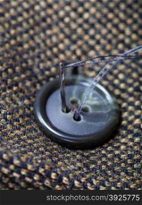 attaching of button to green tweed by needle close up