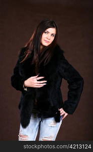 attracive young woman in a fur coat and jeans on browm background