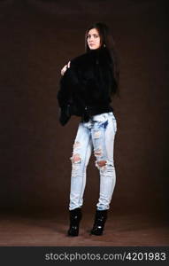 attracive young woman in a fur coat and jeans on brown background