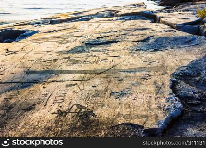 Attraction of Karelia is Onega petroglyphs on the sunset - prehistoric rock engravings (4th-2nd millennia BC) carved on the granite shore of the lake on the cape Besov Nos.. Onega Petroglyphs On The Cape Besov Nos