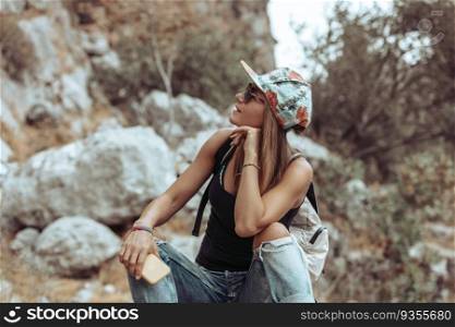 Attractive active female resting on the stone in the mountainous park. Trekking in summer day. Happy healthy lifestyle.. Pretty woman sitting in the park