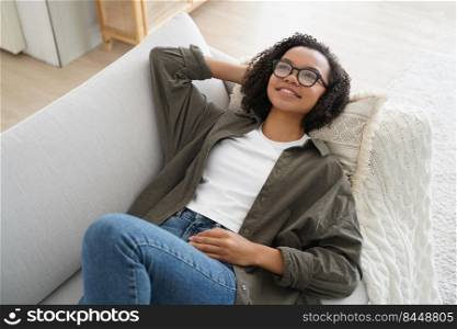 Attractive african american girl dreams. Lady relaxing on couch at home. Young happy woman is smiling. Teenager is enjoying lazy weekend morning and leisure. Comfort and cosy home concept.. Attractive african american girl dreams. Lady relaxing on couch at home. Comfort and cosy home.
